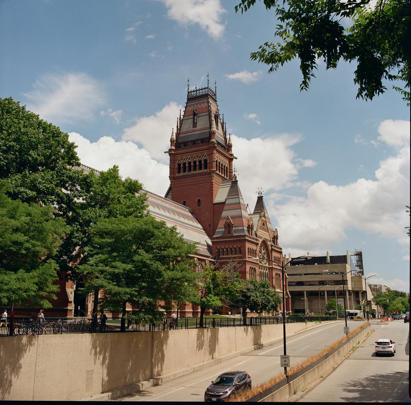 An ornate red brick tower above a tree-lined street under a blue sky.