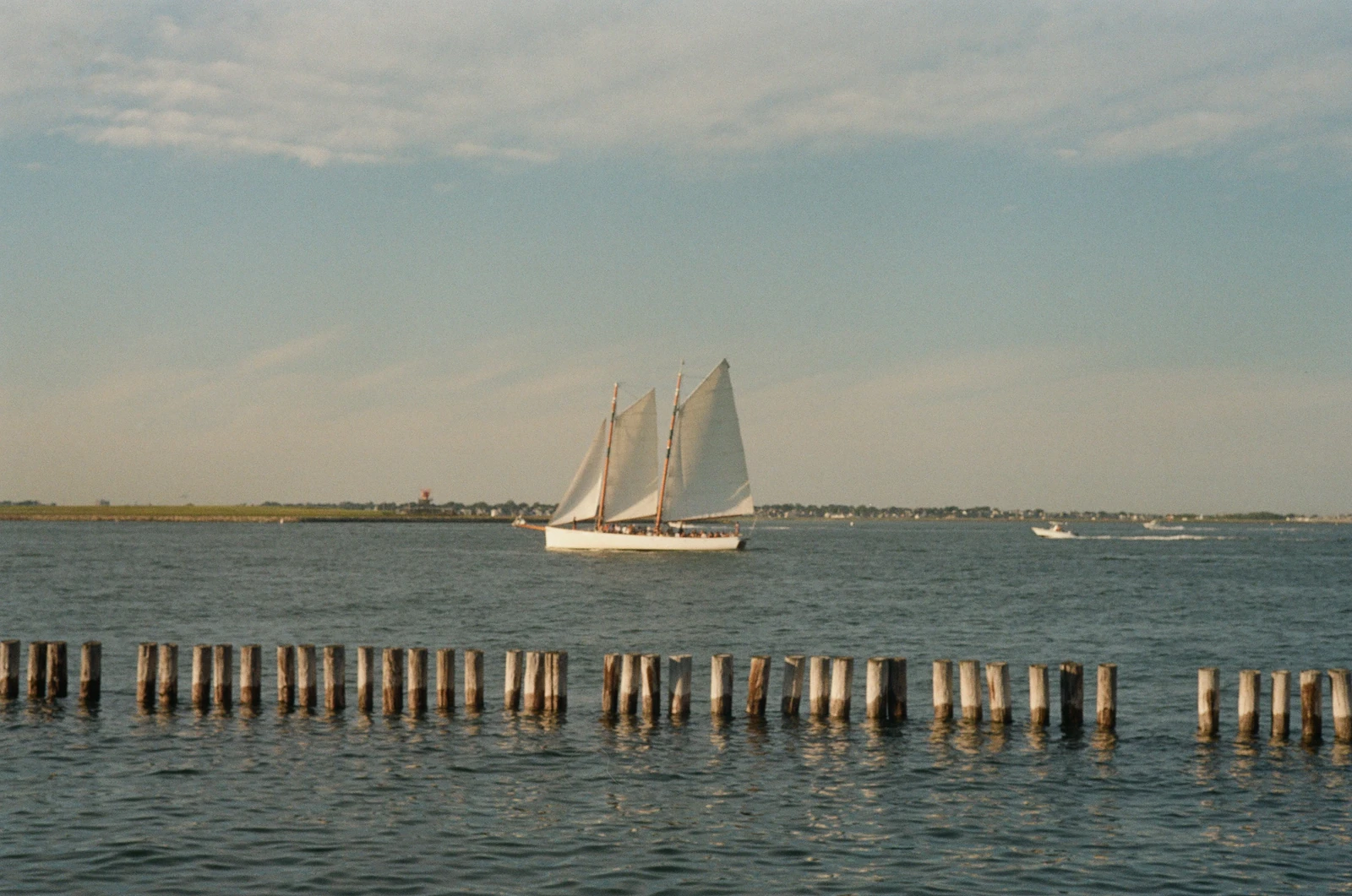 A white sailboat on the water beyond a row of wooden posts.