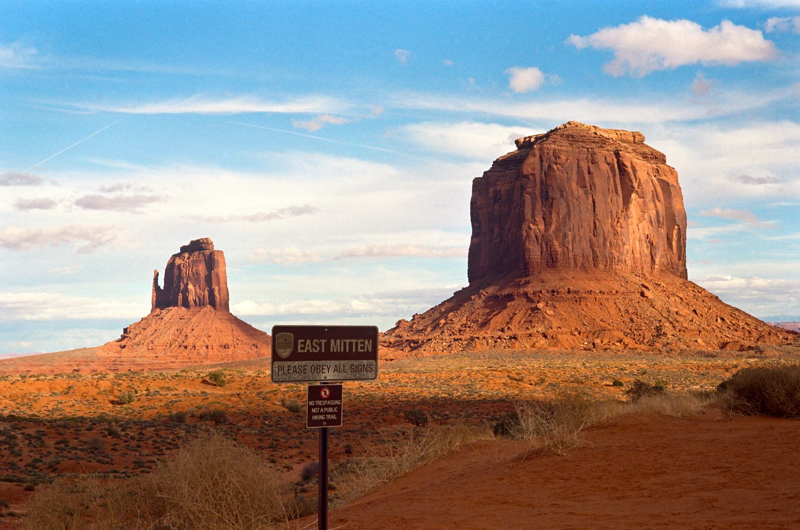 Sandstone buttes in a desert landscape beneath a blue sky with an East Mitten sign.